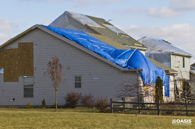 House covered with blue tarps and temporary panels after storm damage