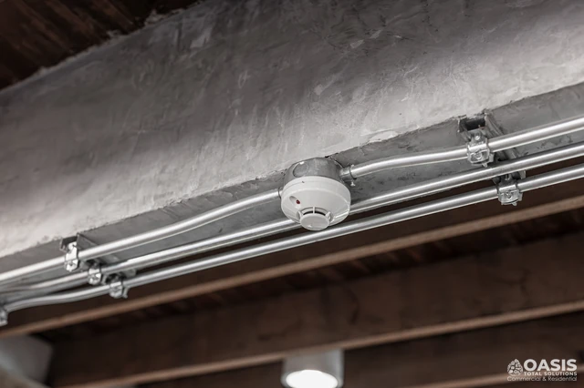 Hard-wired smoke detector mounted on a concrete beam with conduit