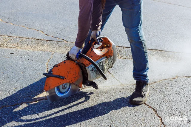 Worker saw-cutting asphalt to repair cracks