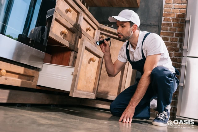 Pest control inspection under kitchen cabinets with a flashlight