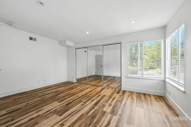 Bright bedroom with corner windows and mirrored closet after renovation