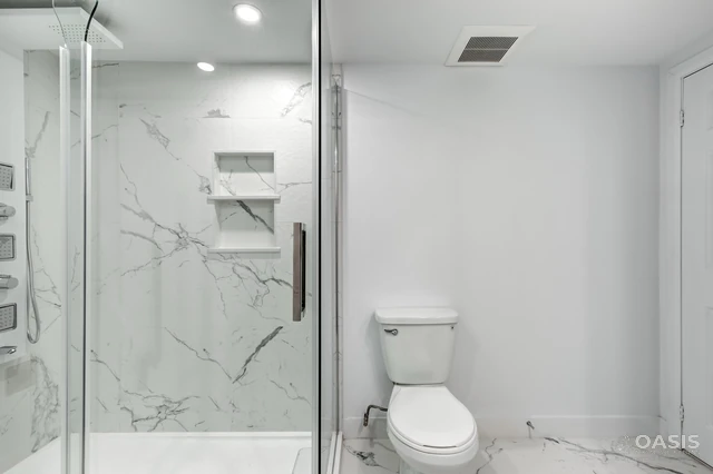 Bathroom remodel featuring frameless shower and marble-pattern tile