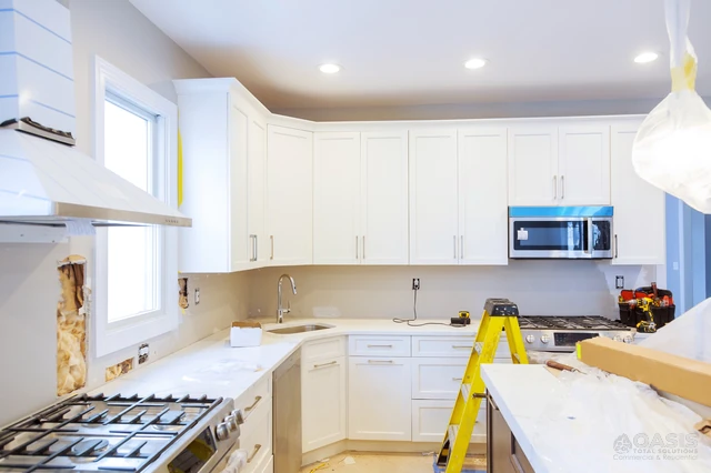 L-shaped kitchen installation with white cabinets and tools on site