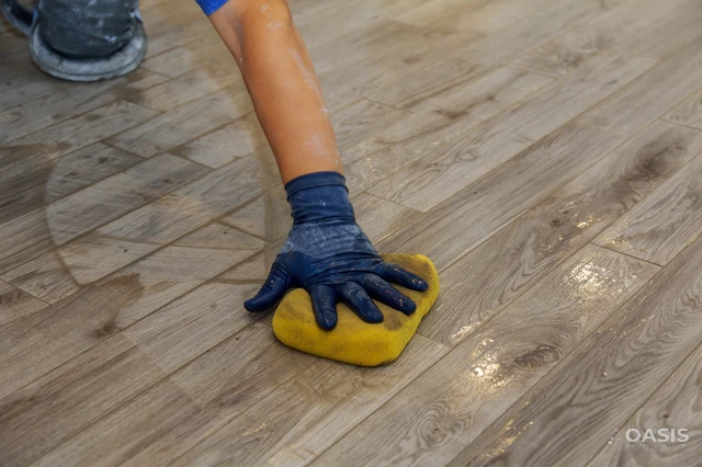 Gloved hand wiping new wood-look flooring with sponge