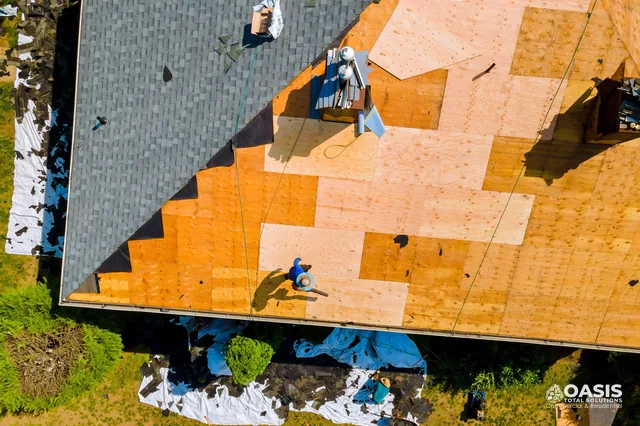Aerial view of a roof replacement with new plywood sheathing and shingles being removed