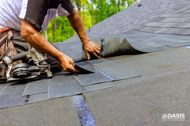Roofer installing architectural asphalt shingles with nail gun nearby