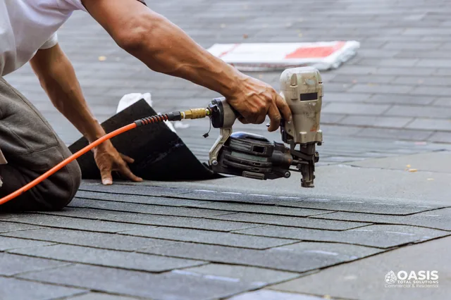 Roofer placing the next shingle while holding a pneumatic nailer
