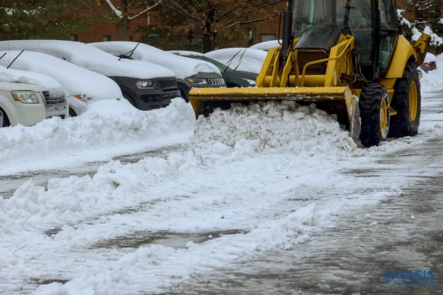 Backhoe pushing snow between parked cars