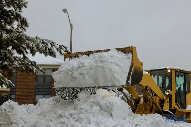 Front loader lifting a large snow pile near apartments