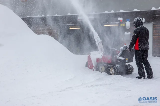 Operator using a snow blower in heavy snowfall by a building