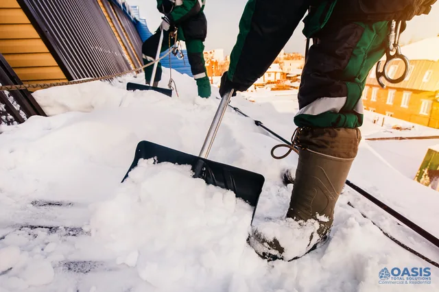 Technicians shoveling snow from a roof with safety lines