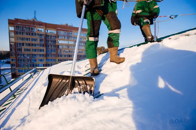 Shovel resting on snowy roof at sunrise near apartments